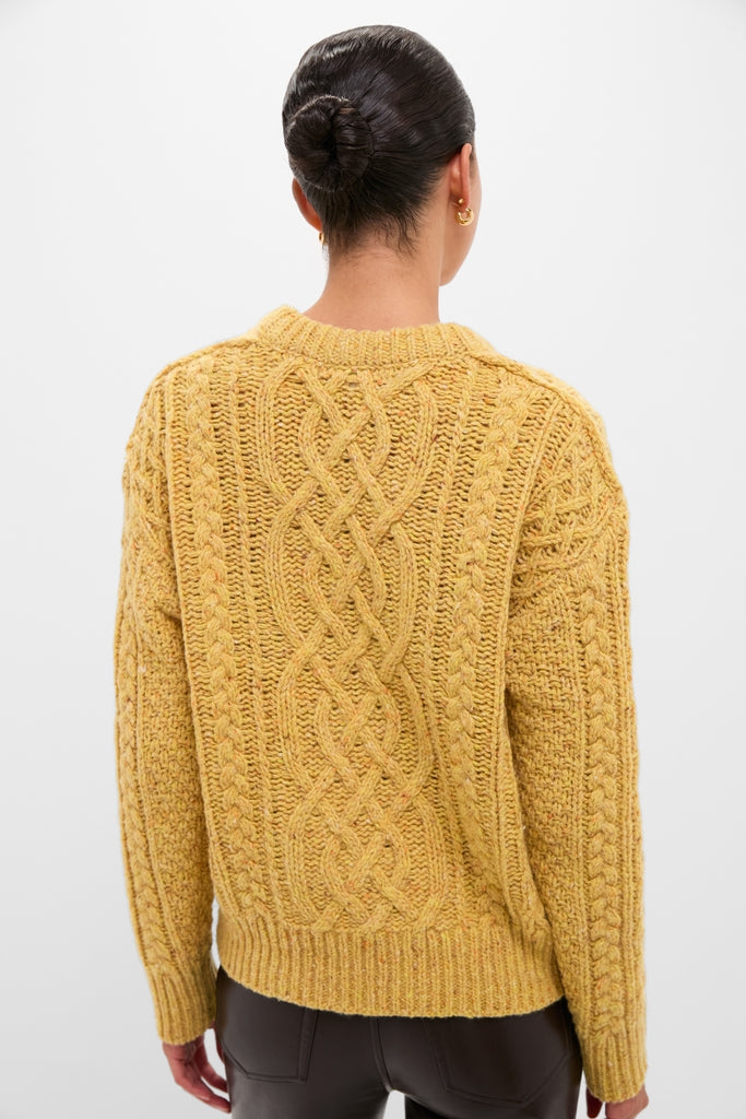 Woman in mustard Sunflower Madelyn Sweater with intricate cable knit, showcasing classic, effortless style with high-end appeal. Dark hair in bun, gold hoop earrings visible.