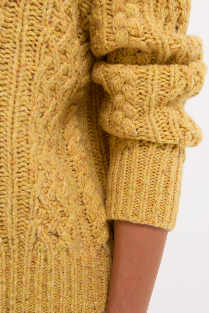 Sunflower Madelyn Sweater's chunky mustard-yellow cable-knit design, showcasing classic texture and ribbed finishes, embodies an effortlessly cool and high-end look.