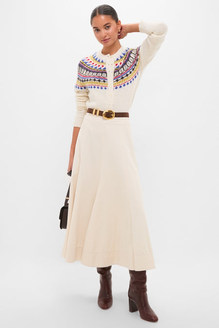 Woman modeling a White Amina Fairisle Sweater, buttoned with a classic fair-isle pattern, cinched by a belt, paired with a flowing skirt and knee-high boots, exuding effortless high-end style.