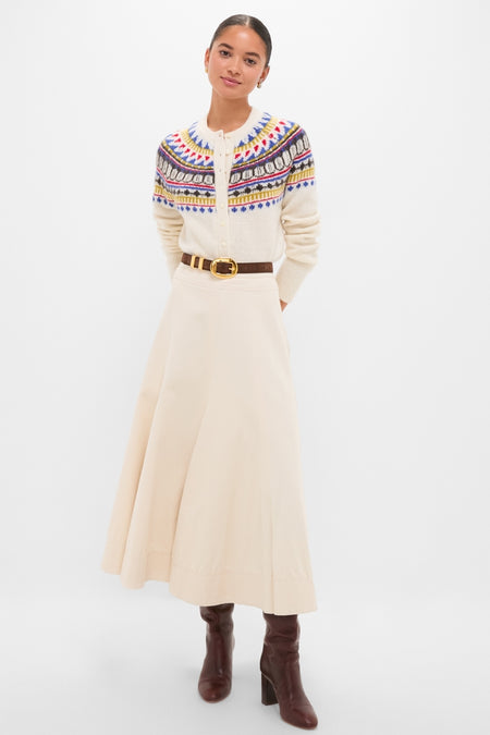 Woman models the classic White Amina Fairisle Sweater with an effortless charm, paired with a high-waisted skirt, dark leather belt, and knee-high boots.