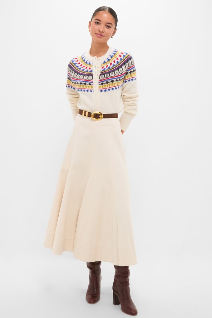 Woman models the classic White Amina Fairisle Sweater with an effortless charm, paired with a high-waisted skirt, dark leather belt, and knee-high boots.