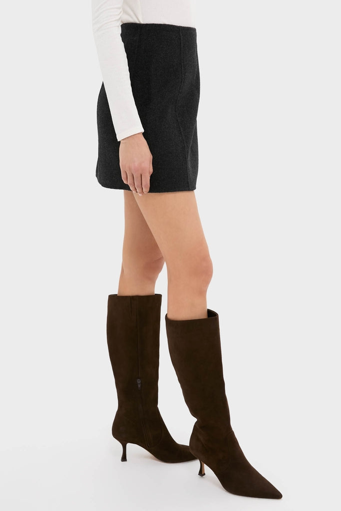 Model wears the Black Naomi Mini Skirt, showcasing its classic A-line silhouette. Paired with knee-high suede boots, this look is effortlessly cool and high-end.