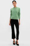 Woman models the classic Meadow Green Cashmere Covered Button Quinn Cardigan, paired with slim-fit black trousers and Mary Jane block-heel shoes, exuding an effortless, high-end style.