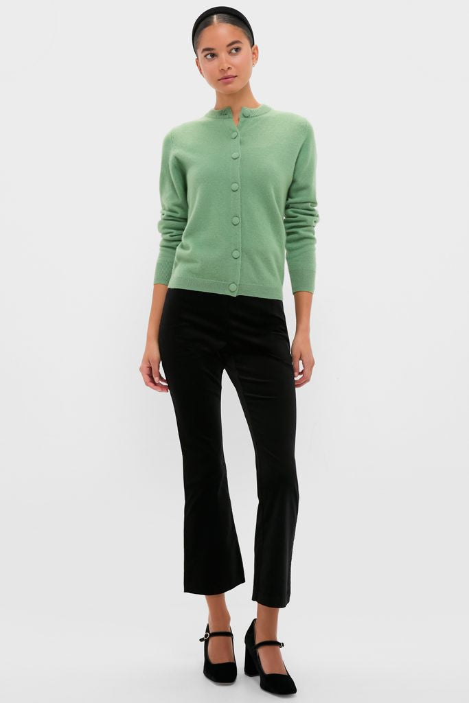 Woman models the classic Meadow Green Cashmere Covered Button Quinn Cardigan, paired with slim-fit black trousers and Mary Jane block-heel shoes, exuding an effortless, high-end style.