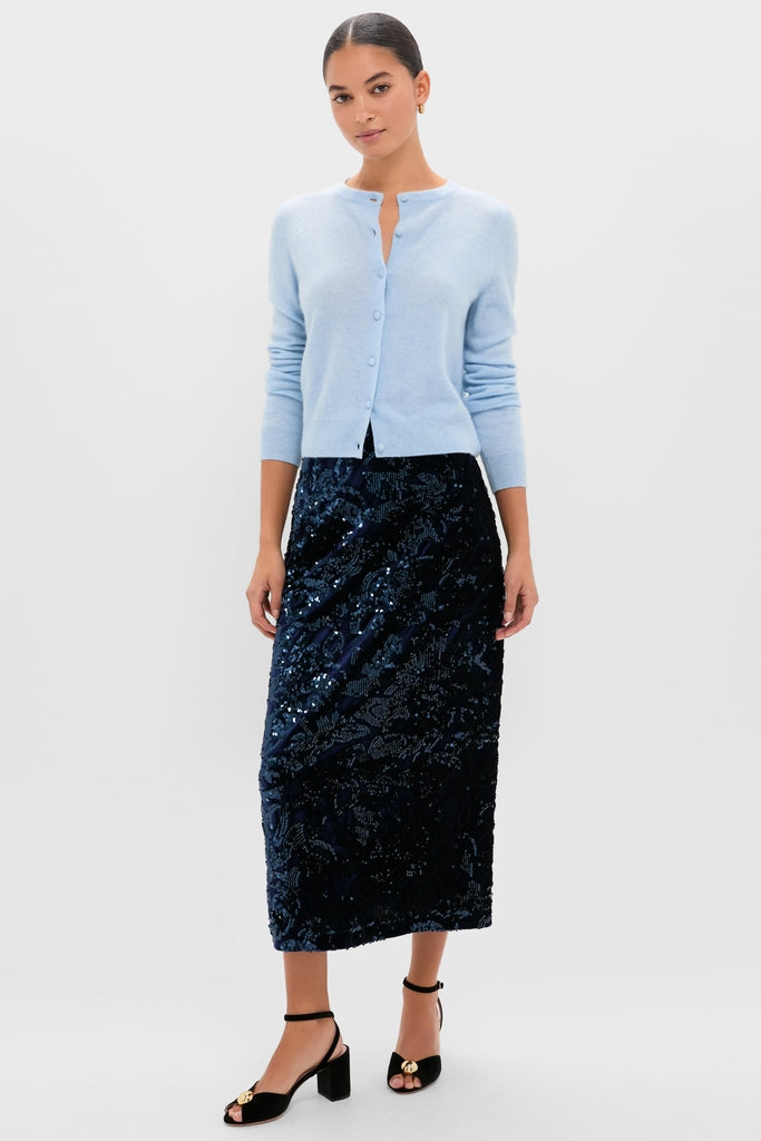 Woman models Ice Blue Cashmere Riley Cardigan with a classic, effortless style, paired with a high-waisted sequin skirt and black block-heel sandals, exuding a fun, high-end look.