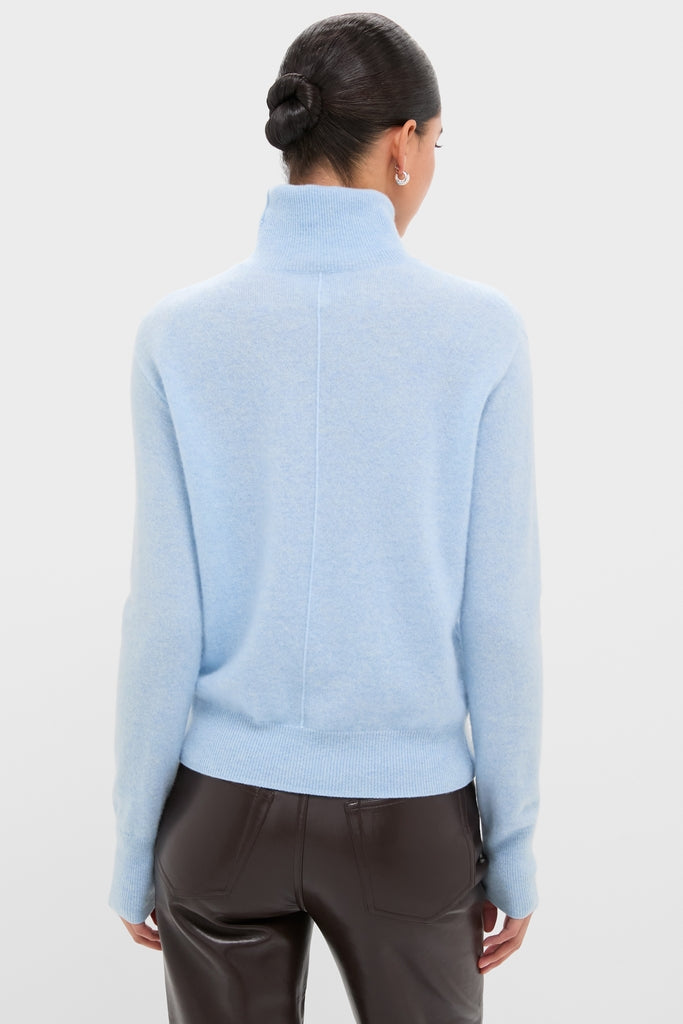 Person wearing a classic Ice Blue Cashmere Turtleneck Sweater, tucked into dark brown leather pants, exuding an effortless, high-end style against a plain backdrop.