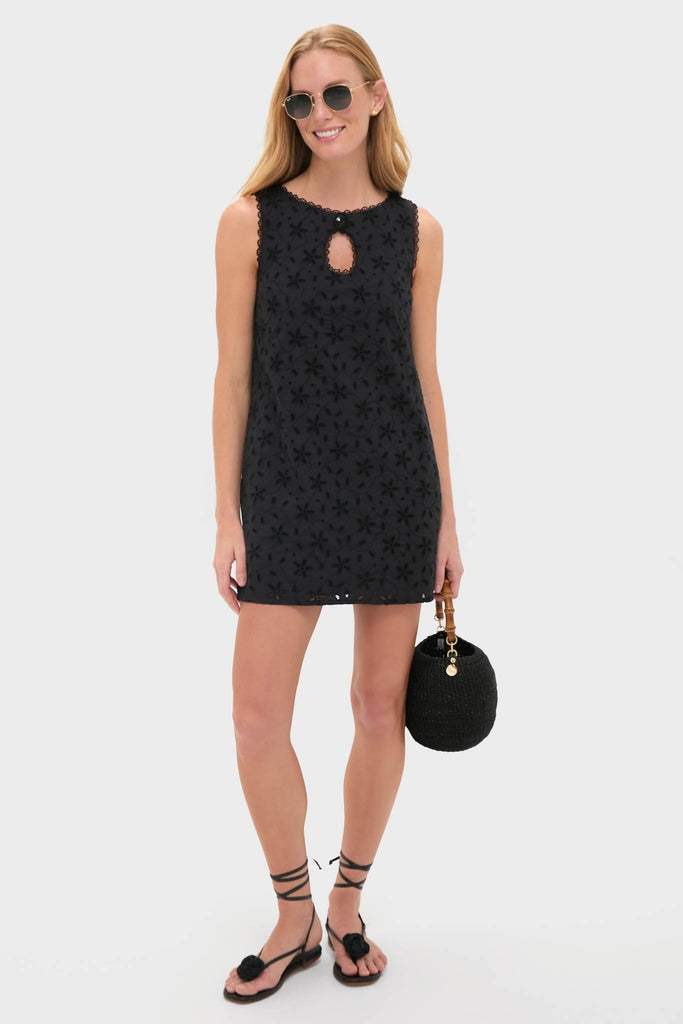 Model in a classic, effortless Black Salma Mini Dress with eyelet details, styled with fun sunglasses, high-end sandals, and a woven handbag, exuding confidence.