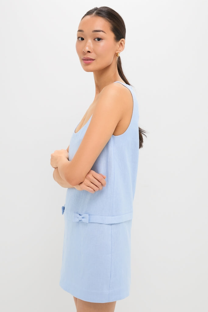 Young woman in profile wearing the Blue Harper Mini Dress, a classic, sleeveless, light-blue garment with bow details, embodying effortless style and high-end fashion for a fun, confident look.