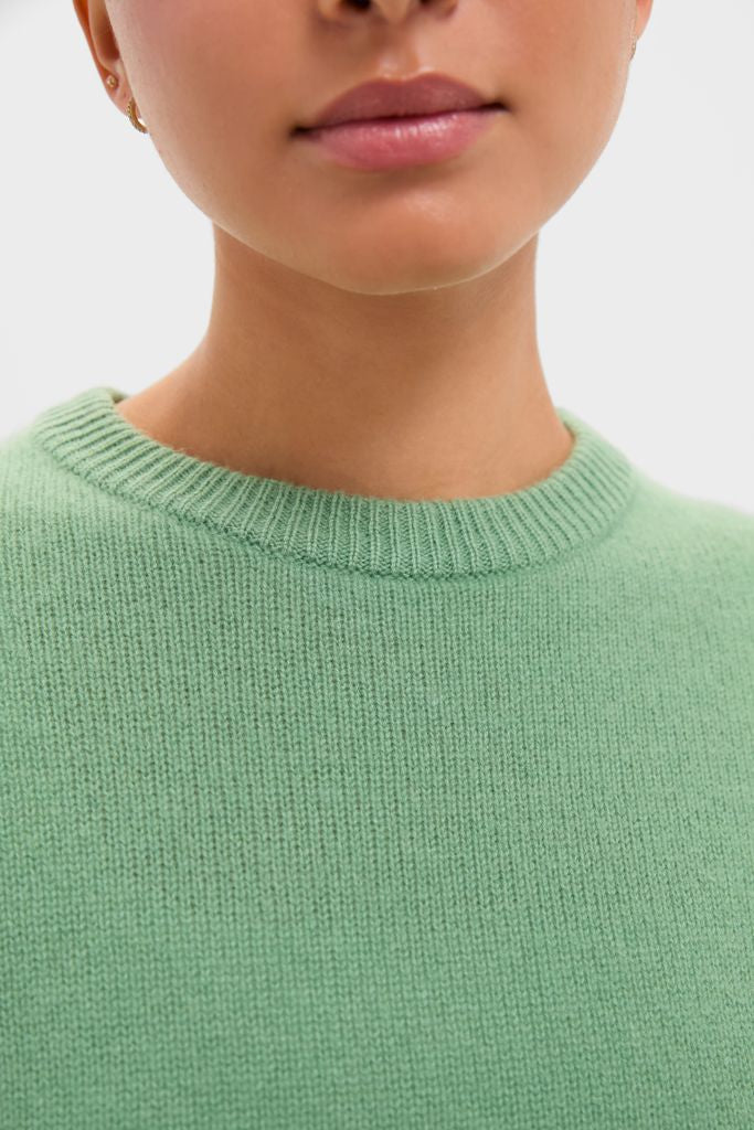Person wearing a classic Meadow Green Cashmere Boyfriend Bodie Crewneck Sweater, showcasing an effortless, high-end style with small gold earrings for a fun, confident look.
