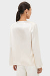 Back view of a woman in a classic, effortless Cream Satin Tatiana Blouse, showcasing its relaxed fit and chic, high-end style against a light background.