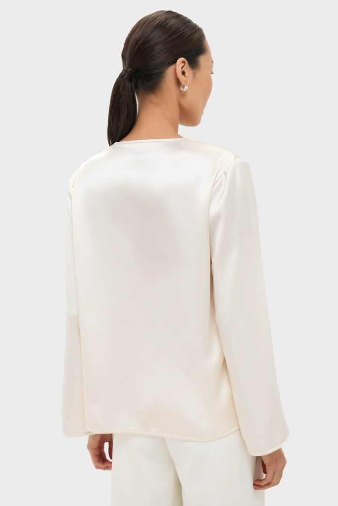 Back view of a woman in a classic, effortless Cream Satin Tatiana Blouse, showcasing its relaxed fit and chic, high-end style against a light background.