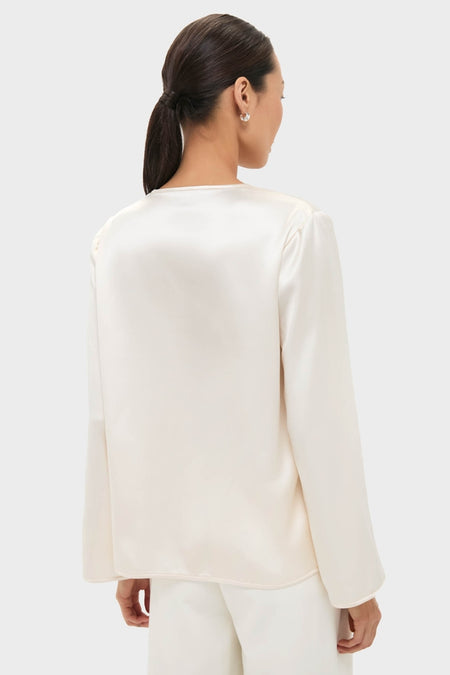 Back view of a woman in a classic, effortless Cream Satin Tatiana Blouse, showcasing its relaxed fit and chic, high-end style against a light background.