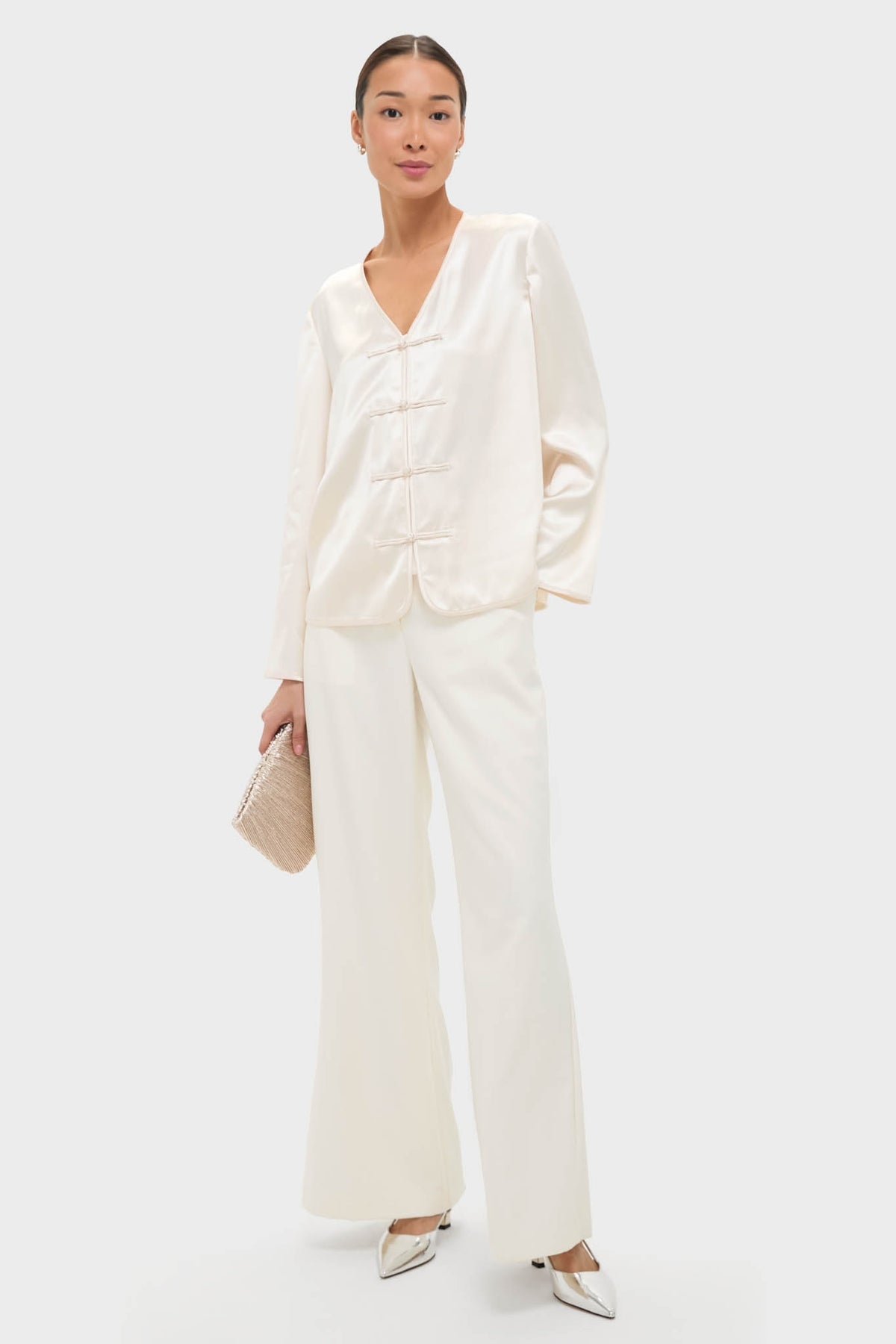 Cream Satin Tatiana Blouse with classic V-neck and chic frog closures styled effortlessly with matching trousers, metallic shoes, and a woven clutch for a high-end, fun look.