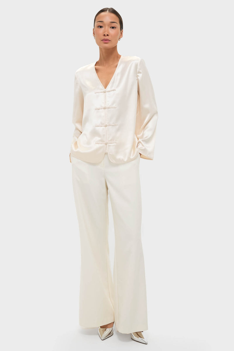 Model wearing the classic Cream Satin Tatiana Blouse with frog closures and a relaxed fit, paired with high-waisted trousers and metallic heels for an effortless, high-end look.