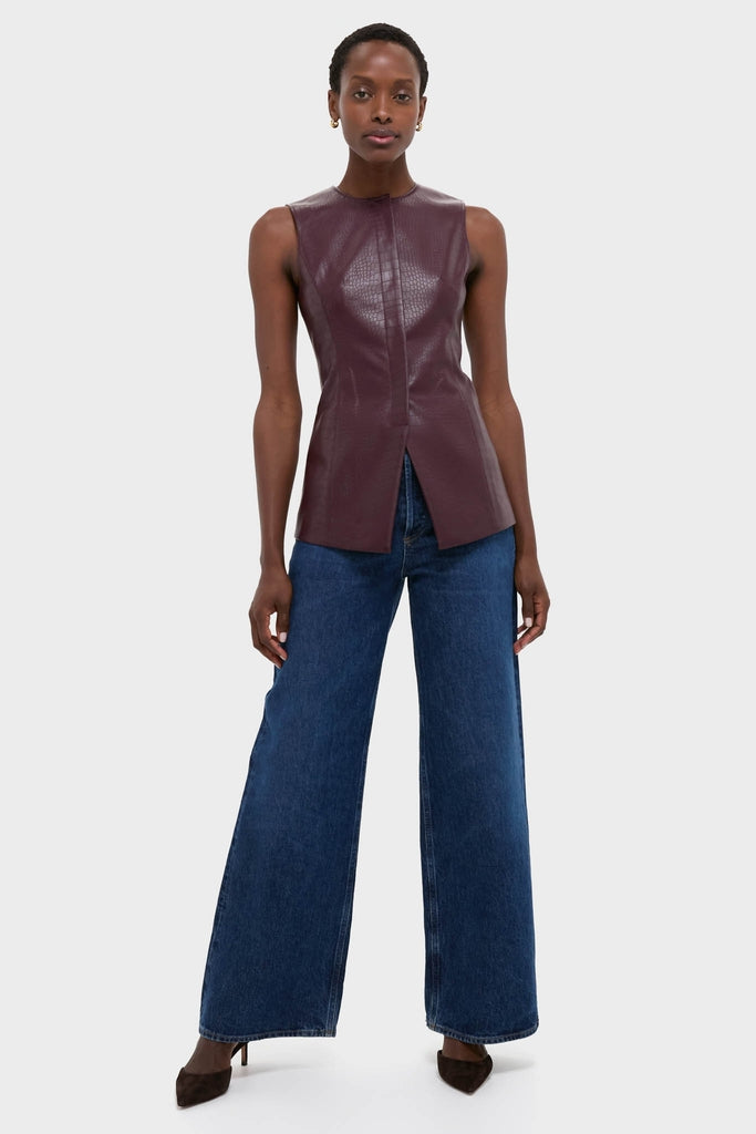 Woman models the classic Plum Stamped Faux Leather Duke Top, a sleeveless, croc-embossed burgundy blouse, paired with high-waisted wide-leg jeans for an effortlessly high-end look.