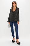 Woman models the Black Satin Tatiana Blouse with V-neck and frog closures, paired with jeans, clutch, and heels for an effortless, high-end, day-to-night chic look.