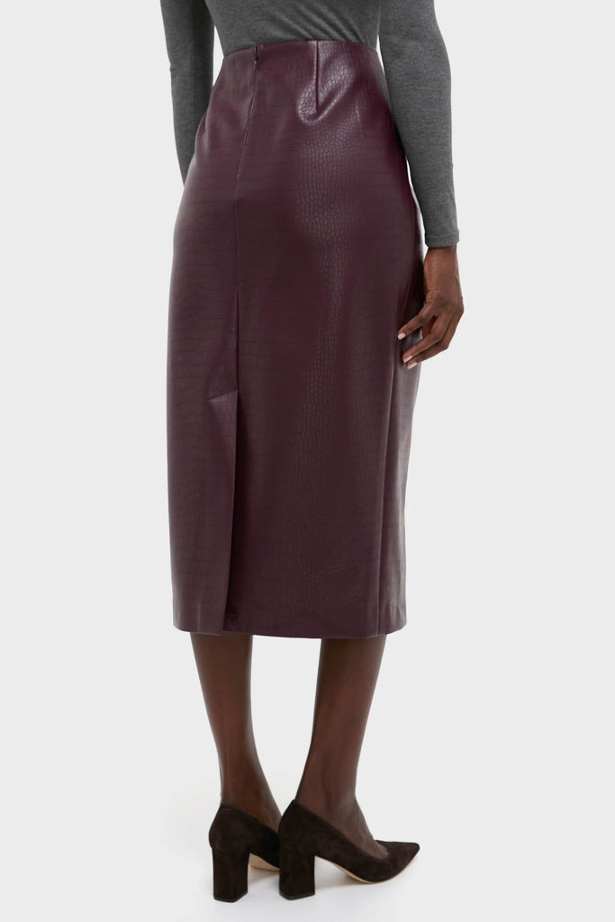 Model showcasing the classic Plum Stamped Faux Leather Ellington Skirt, featuring a high-waisted, calf-length silhouette with croc-embossed texture and back slit, styled effortlessly for high-end versatility.