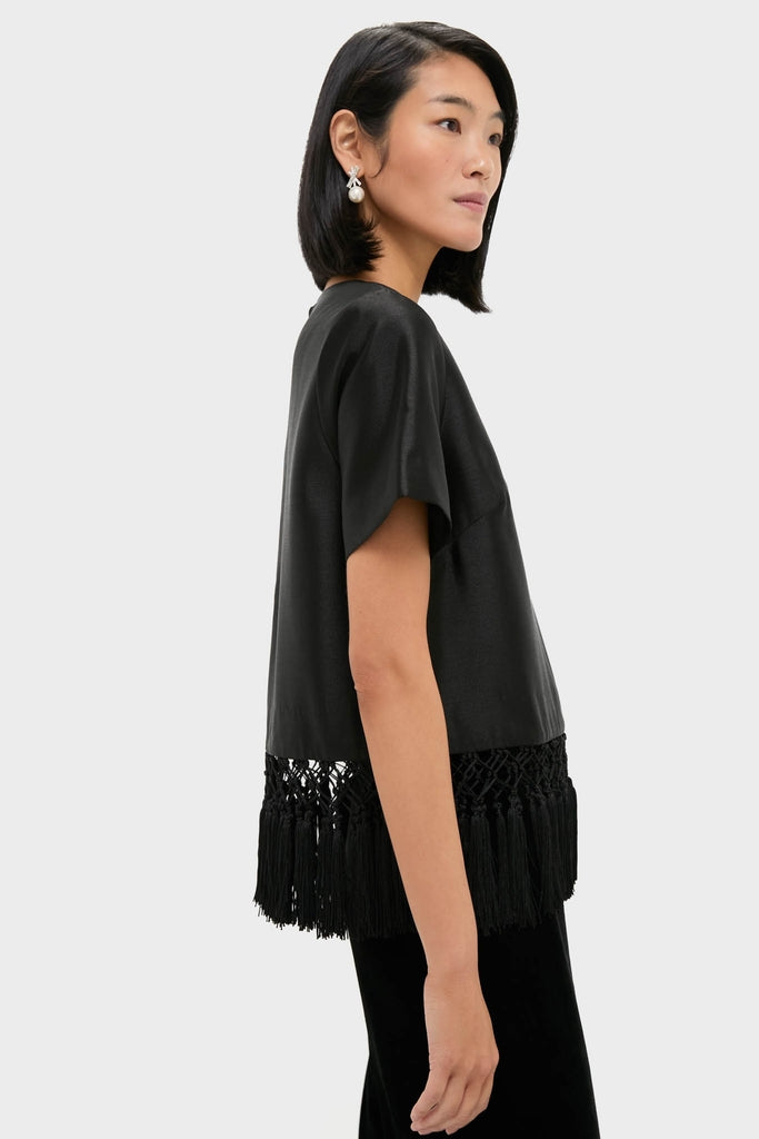 Young woman in a classic Black Dupioni Chadwick Tassel Top with macramé fringe, creating an effortless, high-end look, complemented by drop-pearl earrings for a fun, stylish ensemble.