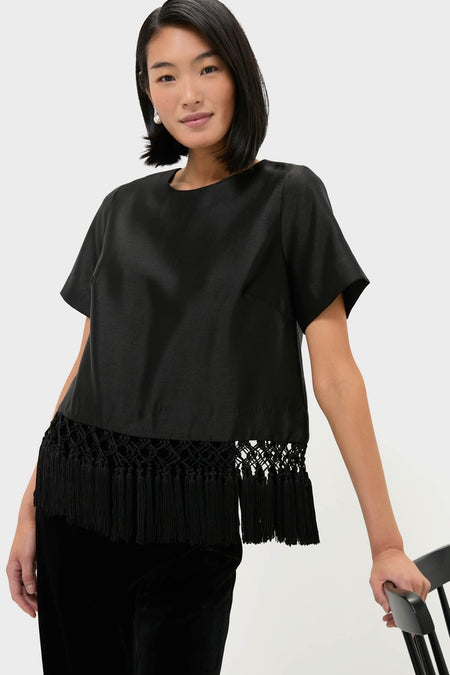 Woman wearing Black Dupioni Chadwick Tassel Top with tassel hem, classic round neck, and relaxed fit, leaning on chair, exuding an effortless, high-end style.