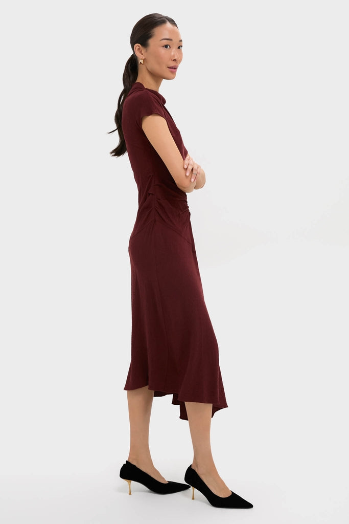 Model in profile wears the Black Cherry Dena Midi Dress, showcasing classic elegance with an effortlessly chic asymmetrical hem, draped neckline, and fun ruched waist detailing.