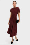 Model in classic Black Cherry Dena Midi Dress with ruched waist, draped neckline, asymmetrical hem; paired with black heels and clutch, exuding effortless, high-end style.