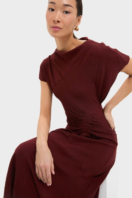 Black Cherry Dena Midi Dress: A classic, effortless burgundy dress with a draped neckline, ruched hip detail, and asymmetrical hem, exuding high-end style and sophistication.