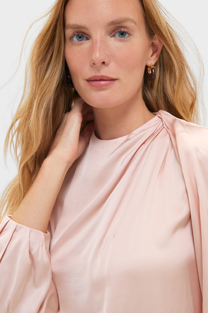 Young woman in the Soft Pink Blush Satin Blaire Top, showcasing classic, effortless elegance with gathered shoulders and gold-tone hoop earrings, exuding a fun, high-end style.