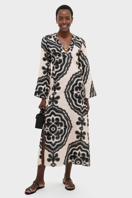 Niku Cream Theodora Column Dress on a model; classic, effortless style with bell sleeves, V-neckline, and abstract motifs, paired with sandals and a woven handbag.