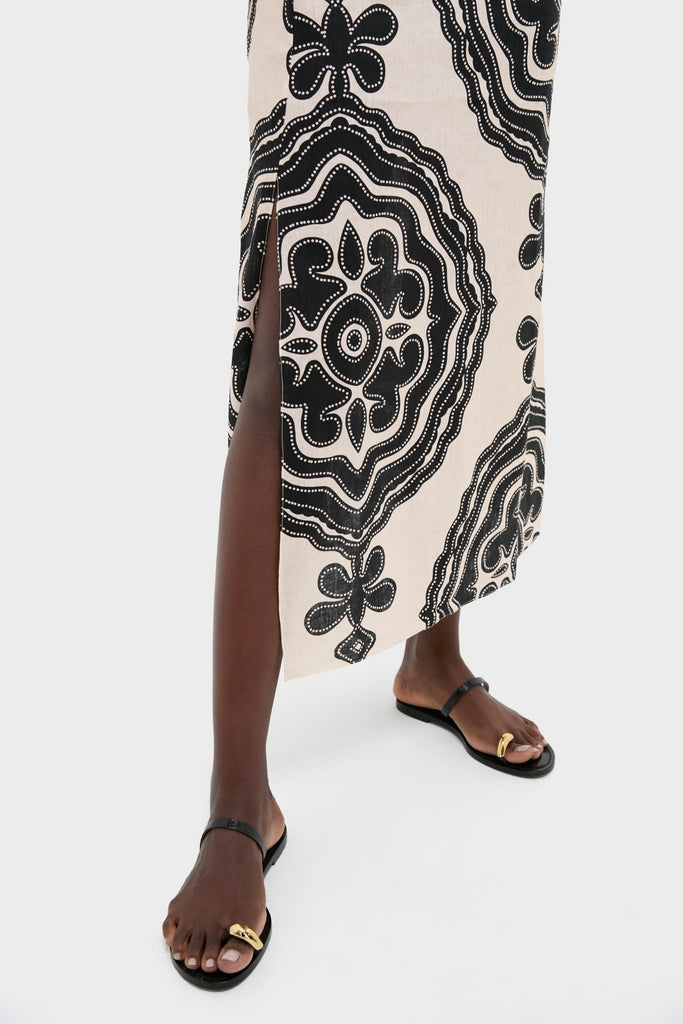 Effortlessly chic Niku Cream Theodora Column Dress with bold motifs and a thigh-high slit, paired with classic black sandals for a high-end, fun look.