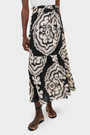 Model wearing the Niku Black Sanaa Skirt, featuring a classic, effortless wrap style with a fun abstract pattern and high-end adjustable tie belt. Paired with sandals.