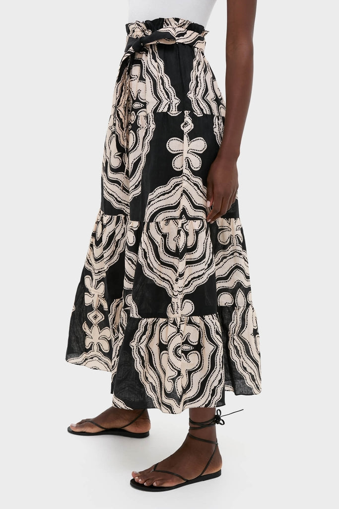 Woman in Niku Black Sanaa Skirt with paper-bag waist and ruffled tiers, paired with black sandals. This classic, high-end piece offers an effortless, fun, and adjustable fit.