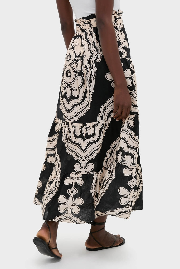Model wearing classic Niku Black Sanaa Skirt with abstract print, effortlessly styled with sandals and a white top, highlighting its adjustable tie belt and button-front closure.