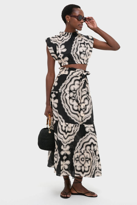 Model wears Niku Black Sanaa Skirt, featuring an effortless, high-end graphic print with a classic tie waist. Paired with matching top, black handbag, sandals, and sunglasses.