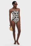 Model wearing Niku Black Elene One Piece swimsuit with abstract pattern, showcasing classic, effortless style. Features wide scoop neckline, adjustable straps, and high-end detailing. Holding straw hat, exuding fun.