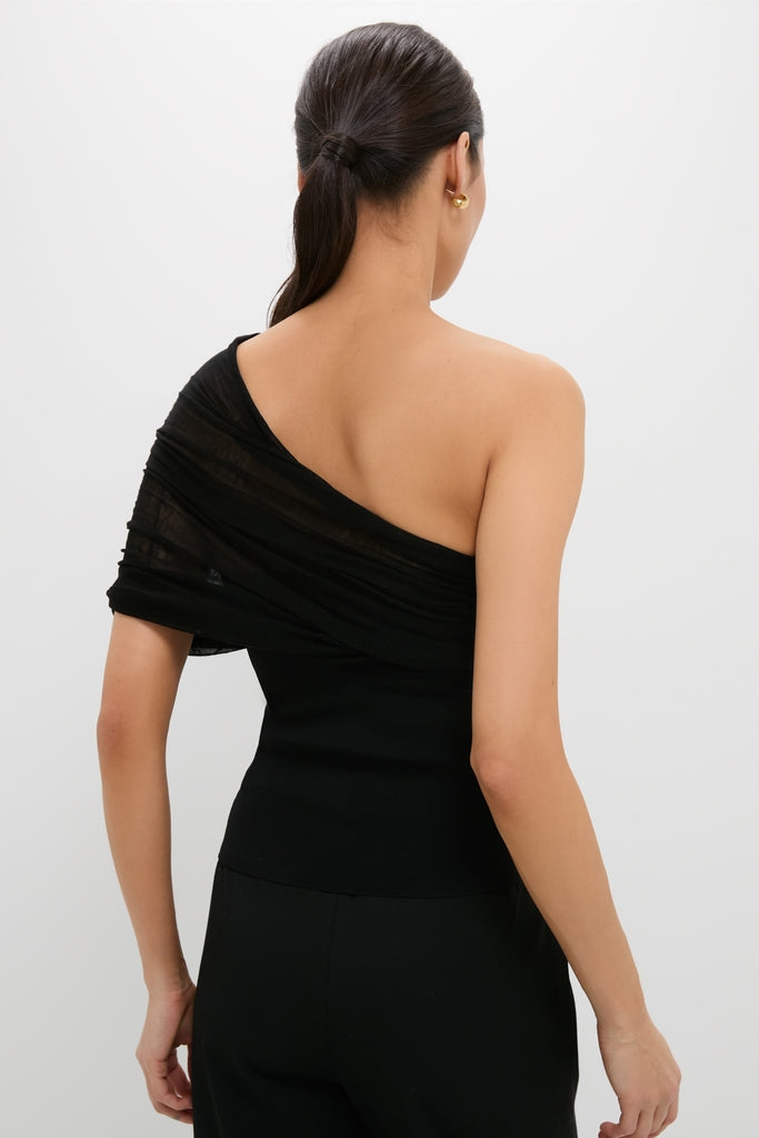 Woman in a classic Black Satterly Top with a one-shoulder design, showcasing an effortless, high-end style, paired with a gold hoop earring.