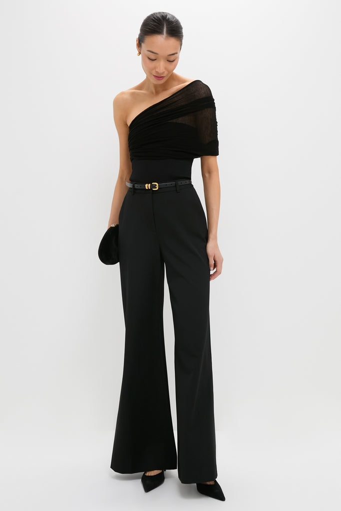 Model in a classic, high-end Black Satterly Top, effortlessly styled with flared trousers, pointed heels, and a clutch, embodying fun sophistication with a relaxed pose.