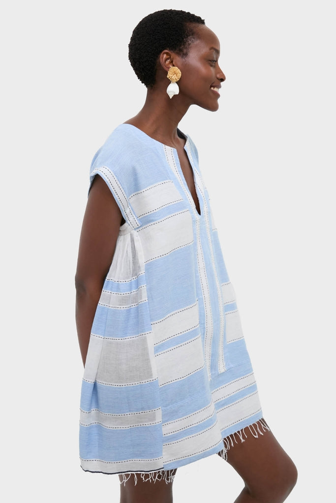 A model in profile wearing the classic, effortless Debre Sky Elina Caftan, featuring a V-neck, cap sleeves, and fringe hem, paired with gold drop earrings.