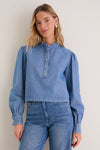 A young woman models the Indigo Denim Margot Top, featuring classic puffed sleeves and a stand collar, exuding effortless, high-end style.