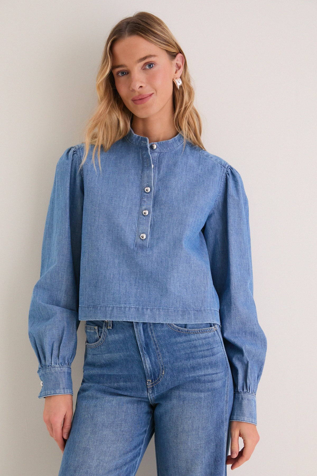 A young woman models the Indigo Denim Margot Top, featuring classic puffed sleeves and a stand collar, exuding effortless, high-end style.