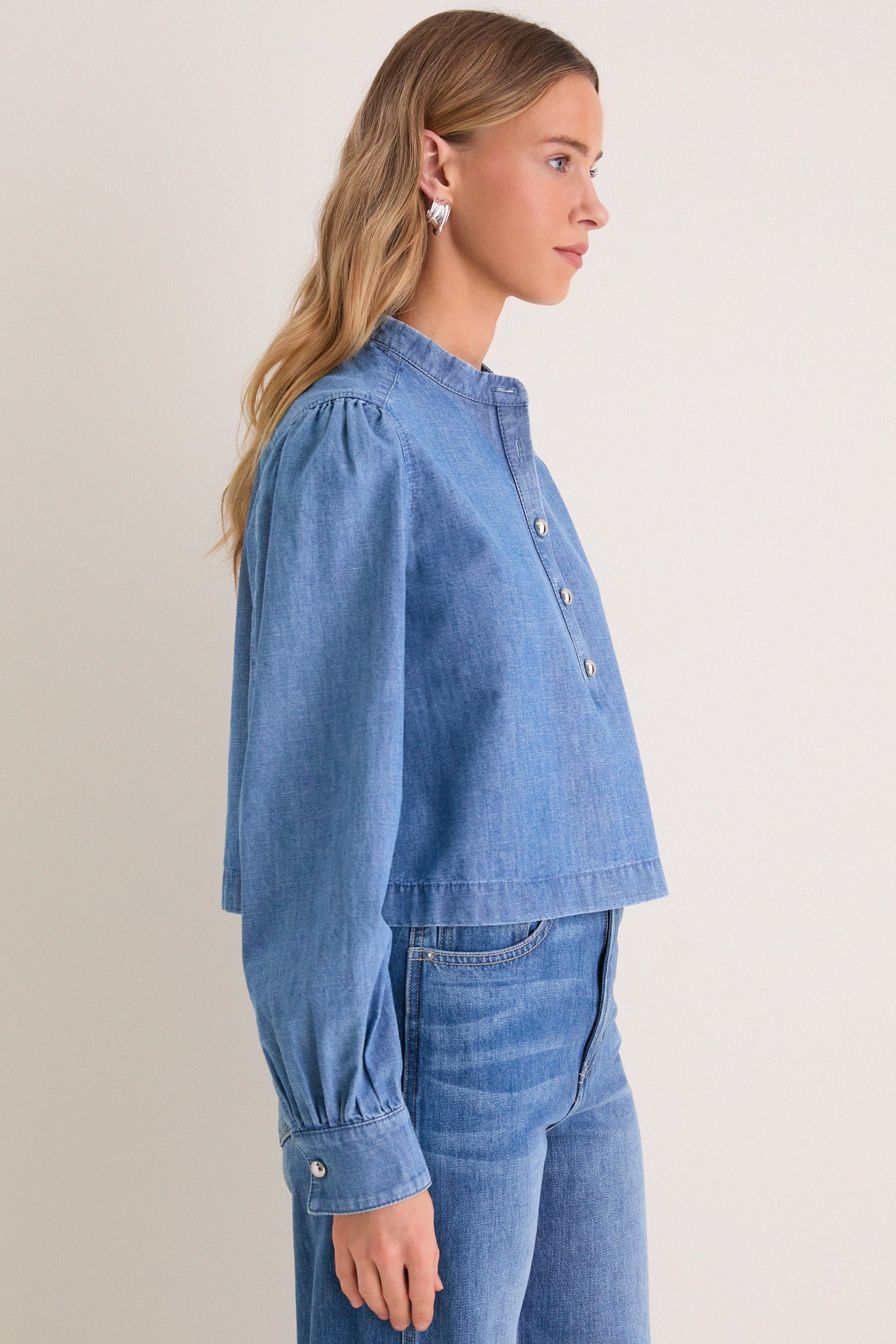 Model wearing Indigo Denim Margot Top, a classic, effortlessly stylish chambray blouse with blouson sleeves and silver buttons, embodying high-end, fun fashion.
