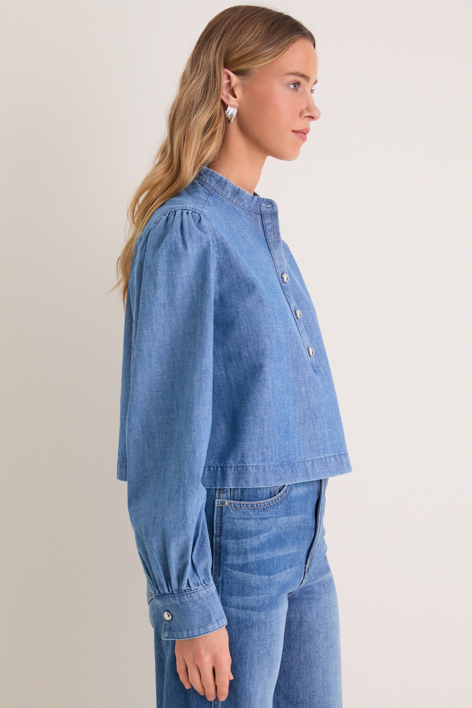 Model wearing Indigo Denim Margot Top, a classic, effortlessly stylish chambray blouse with blouson sleeves and silver buttons, embodying high-end, fun fashion.