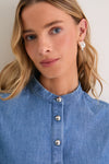 Young woman wearing the Indigo Denim Margot Top with sculptural silver hoop earrings, showcasing its classic, effortless style with gold hammered buttons and subtle balloon sleeves.