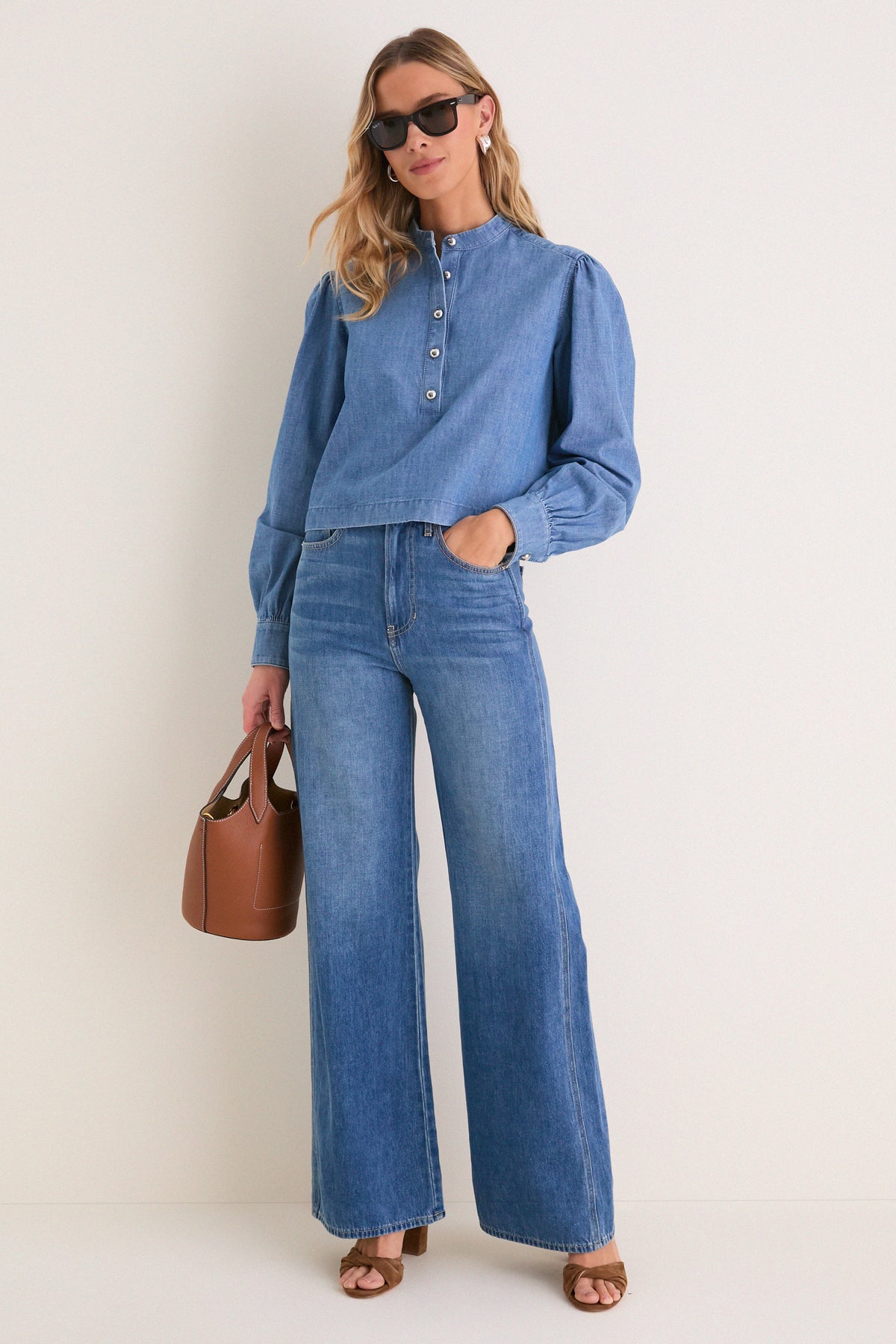 Model showcases the Indigo Denim Margot Top, a classic, effortlessly stylish blouse with a mandarin collar and button placket, paired with matching jeans and chic accessories.