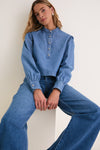 Young woman in an Indigo Denim Margot Top, showcasing a classic high-end design with effortless style, featuring silver buttons and a modern, fun cropped fit.