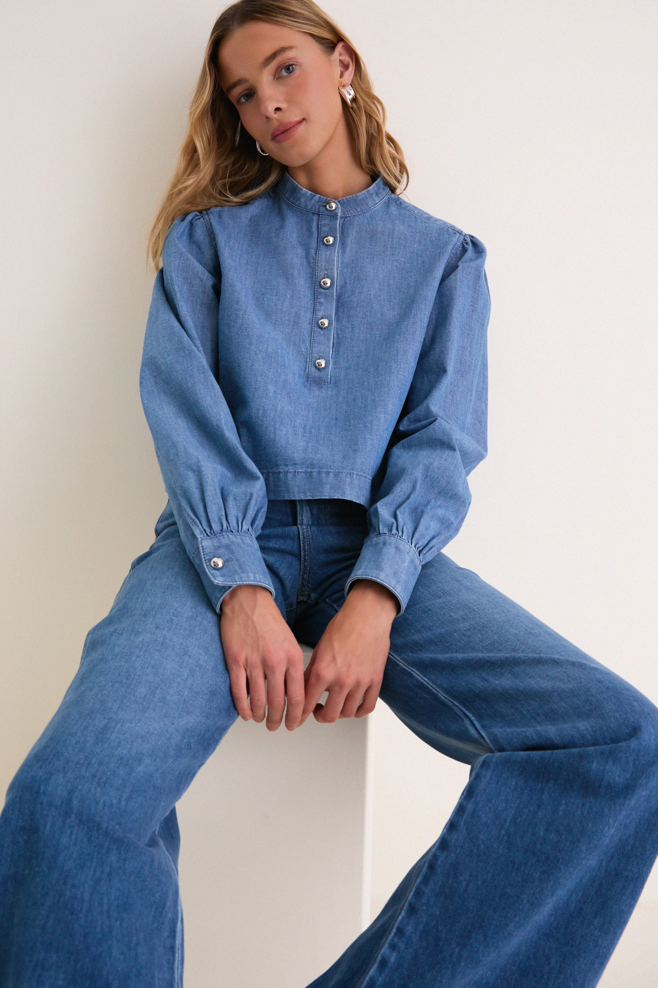 Young woman in an Indigo Denim Margot Top, showcasing a classic high-end design with effortless style, featuring silver buttons and a modern, fun cropped fit.