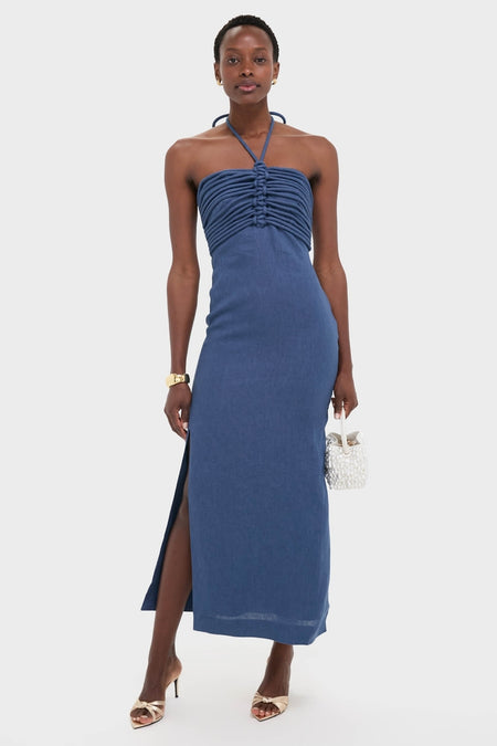 Model in the Indigo Mezcalitos Midi Dress with a classic, effortless ruched bodice, halter neck, and side slit, accessorized with gold heels and a beaded bag.