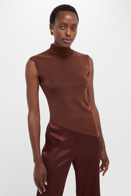 Model wearing the classic Rust Edith Top, an effortless sleeveless brown turtleneck with an asymmetrical hem, paired with high-end glossy burgundy trousers and a bold earring.