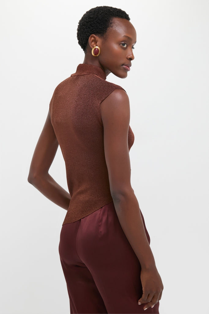 Woman in profile wearing the Rust Edith Top, a sleeveless metallic-shimmer piece, paired with deep burgundy trousers and gold-trimmed earrings, showcasing a classic and effortless style.