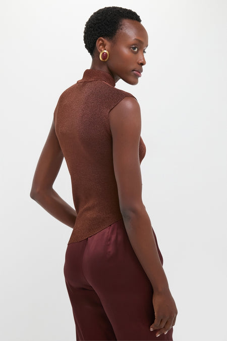 Woman in profile wearing the Rust Edith Top, a sleeveless metallic-shimmer piece, paired with deep burgundy trousers and gold-trimmed earrings, showcasing a classic and effortless style.