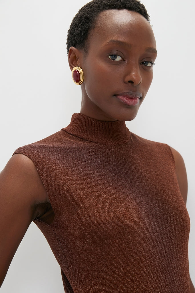 A poised woman models the classic Rust Edith Top, exuding effortless style with a sleeveless high-neck design, paired with a high-end statement earring.